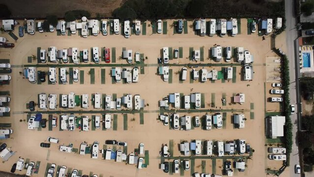 Toma de drone en 4k  de un aparcamiento en un terreno de tierra junto a la playa lleno de caravanas 