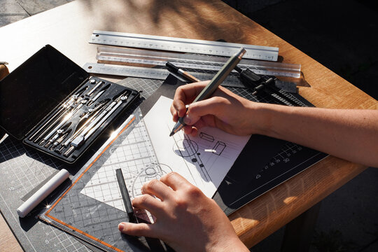 Architect and designer working accurately on a project drawing sketches and technical drafts on paper using professional tools like rulers compass and triangle logo design top view over the shoulder