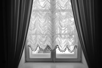 The window of a rich manor house with open dark curtains and light tulle.