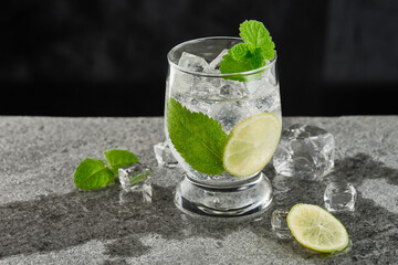 Glass of mojito cocktail with mint leaves and lime pieces on a grey background. Low angle view. Studio shot.