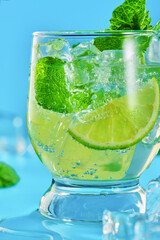 Close-up of one glass with a mojito cocktail on a blue background. Vertical shot from a low angle.