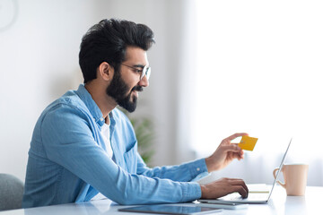 Online Shopping. Cheerful Indian Man Using Credit Card And Laptop Computer