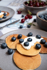 pancakes with blueberries on plates, near cherries and blueberries in bowls