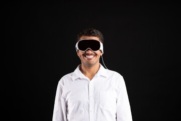 Cheerful brazilian man in shirt wearing vision pro vr glasses, using modern gadget on black studio background