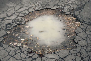 A large puddle of muddy water in the middle of an asphalt road