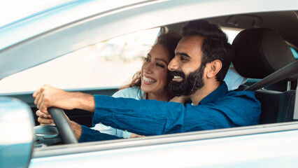 Joyful arab couple driving their new car and exploring roads, sitting with opened window