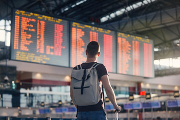 Traveling by airplane. Man walking with backpack and suitcase walking through airport terminal and looking at departure information.. - 624135342