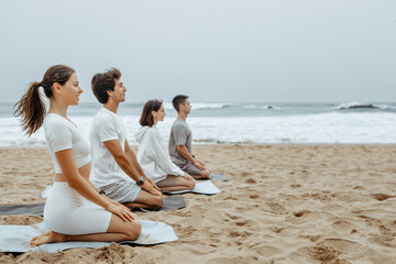 Fototapeta na wymiar Unearthing inner peace. Young men and woman practicing yoga on the beach, sitting on mats on ocean shore, free space