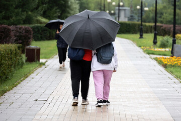 Couple with one umbrella walking on a street. Rainy weather in city, summer storm