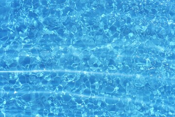 Blue water with ripples on the surface. Defocus blurred transparent blue colored clear calm water surface texture with splashes and bubbles. Water waves with shining pattern texture background.