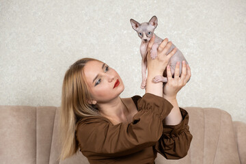 A woman holds a small Canadian Sphynx kitten in her hands. Love for pets, cat's day.