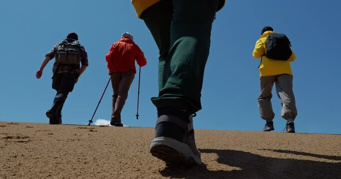 Travel group of friends together goes in desert area slow motion. Tourists foots in trekking boots stepping close up back view