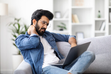 Tired Indian Man Suffering Neck Pain While Working With Laptop At Home