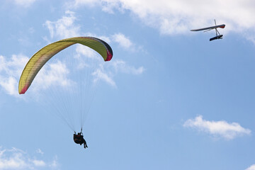Tandem Paraglider and hang glider flying in a blue sky	
