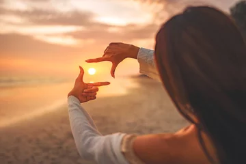Fotobehang Travel planning concept, Close up of tourist woman hands making frame gesture on the sea beach with sunset, Female capturing the sunrise. © oatawa