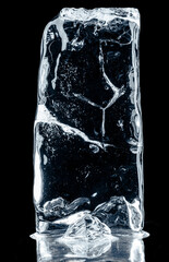 Crystal clear natural ice block with air bubbles and cracks on black reflective surface