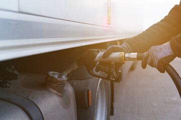 A man holds a gun in his hands, which he inserted into the neck of the fuel tank, refuels the truck.