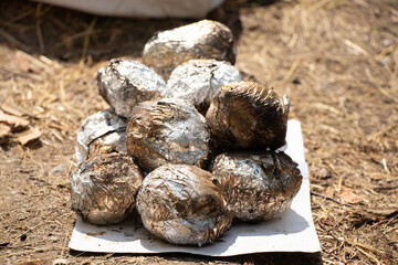 Potatoes in foil baked on the grill in the coals in the summer at a picnic lie on paper on the ground in a pile, food on the grill, lunch