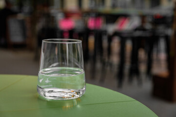 Glass of still water on the table of a city cafe terrace on warm summer evening. Street in bokeh.