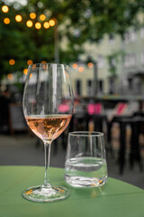 Glass of rose wine and water on a table of a city cafe terrace on summer evening. Street in bokeh.