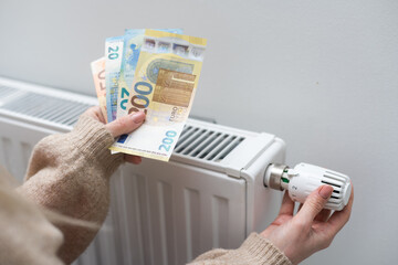 Woman holding cash in front of heating radiator. Payment for heating in winter