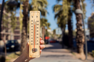 Hot weather. Thermometer in hand in front of street with trees and palms during heatwave. High temperature concept