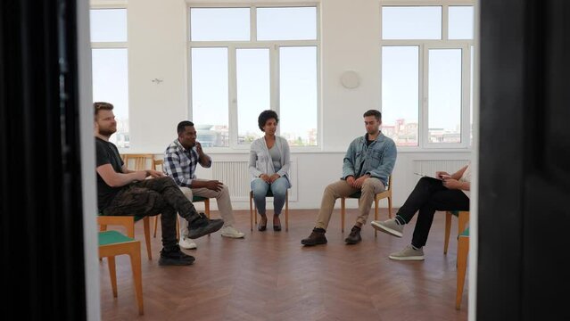 Zoom in shot of multicultural support group during meeting with professional mature male therapist. Group of men and women looking pensive during team counselling session. Shooting in slow motion.