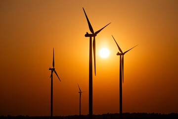Silhouettes of wind turbines against the setting sun