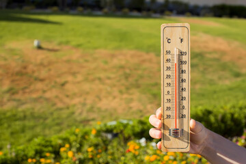 Hot weather. Thermometer in hand in front of dry grass during heatwave. High temperature concept