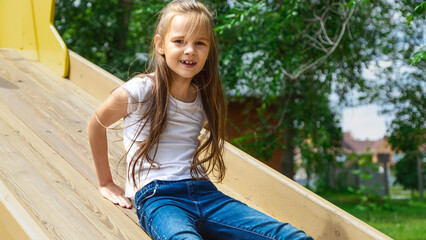 A cute little girl is playing in the children's yard. Healthy summer fun for kids. Child girl climbs down the street at the playground. Children's outdoor games.