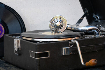 A black music record plays on an old gramophone. There is a round metal shiny pickup with a needle and a handle for twisting the spring. Vintage. Background.