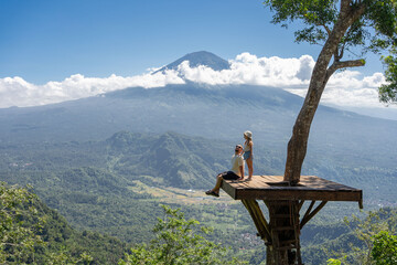 Father and daughter tourists enjoying travel around Bali island , Indonesia. They stands on photo location on the tree with view on Agung Mountain