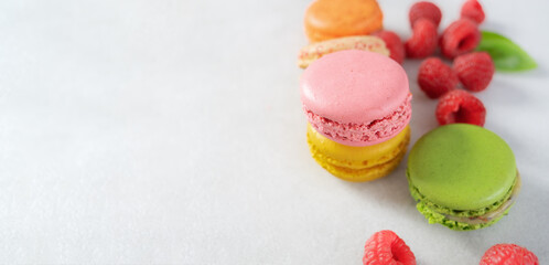 Colored macaron, French macaroon, French traditional cookies and raspberries on a light background with copy space. Dessert for tea, sweet breakfast