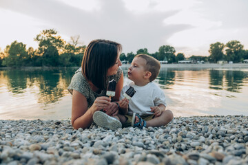 Woman with her son enjoying family time walking on the lake together , eating ice cream. Happy family parent with little child boy kid enjoy outdoor lifestyle. Mum and sun eat ice-cream