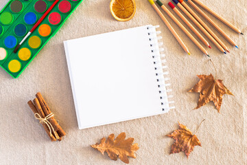 Autumn composition with blank sketchbook, watercolor palette, pencils, fallen dry leaves, cinnamon...