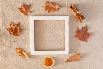 Autumn composition with an empty frame in the center, around autumn dry leaves, dried orange, cinnamon on a background of linen fabric. Flat lay, copy space, fall concept.