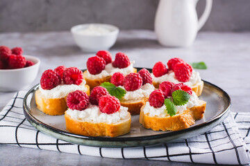 Appetizing crostini with ricotta, raspberries and mint on a plate on the table