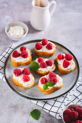 Sweet bruschettas with curd cheese and raspberries on a plate on the table vertical view