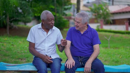 Two diverse senior talking and laughing sitting on park bench in Brazil. Candid authentic people real life laugh and smile in old age retirement golden years