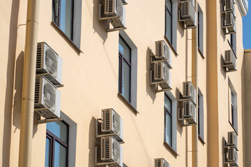 Facade of building with many air conditioners on windows in southern hot country. Yellow house exterior on city street. Escape from heat, creating favorable microclimate in urban apartments concept.