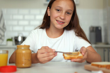 A girl in a good mood making a peanut butter sandwich in the kitchen