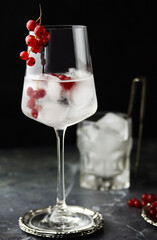 Close up of iced red currant drink. Fresh ice cold fruit cocktail in wine glass, refreshing summer red currant berry drink with on stone concrete background, front view, copy space. Red currant water