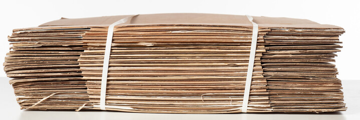 Disassembled cardboard boxes. Cardboard material is fastened with plastic tie. Rolled up carton parcels. Packing material. Cardboard sheets on white background. Concept production investment material