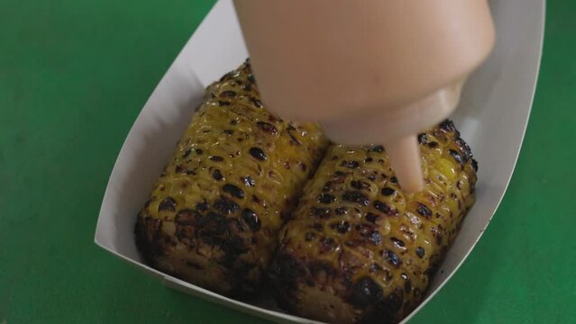 Chef preparing elote street food covering grilled corn with sauce