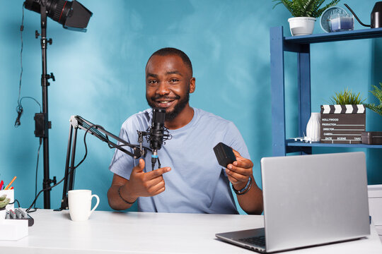 Smiling blogger showing gear for professional videography equipment and talking while recording video. Cheerful vlogger testing and reviewing battery for photography camera