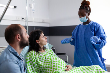 African american surgeron preparing pregnant woman for surgery, explaining childbirth process in...