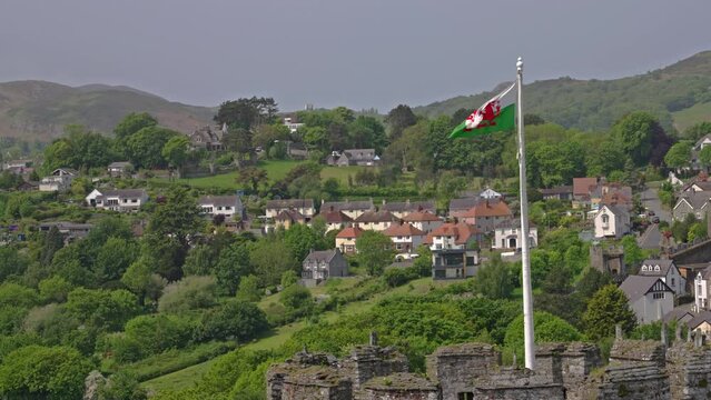 Welsh dragon flag blowing in the wind against a backdrop of a mountain side residential neighborhood, on a spring afternoon, in Conwy, Wales, UK