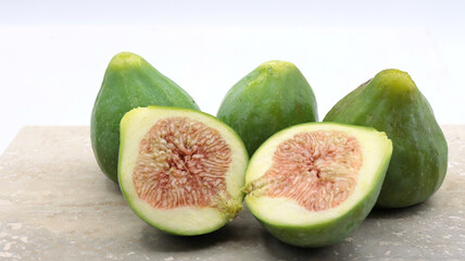 close-up of a group of ripe green figs, one cut in half, on a marble table and white background.