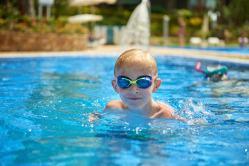 Young boy kid child eight years old splashing in swimming pool having fun leisure activity. Boy happy swimming in a pool. Activities on the pool, children swimming and playing in water, happiness and