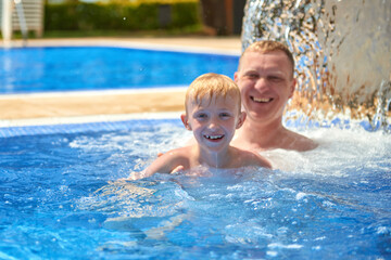 Dad with son splashing in the pool. Father and son in swimming pool on summer vacation. Child with dad playing in pool. Dad and kid in pool at summer day. Leisure and swimming at holidays. Father have
